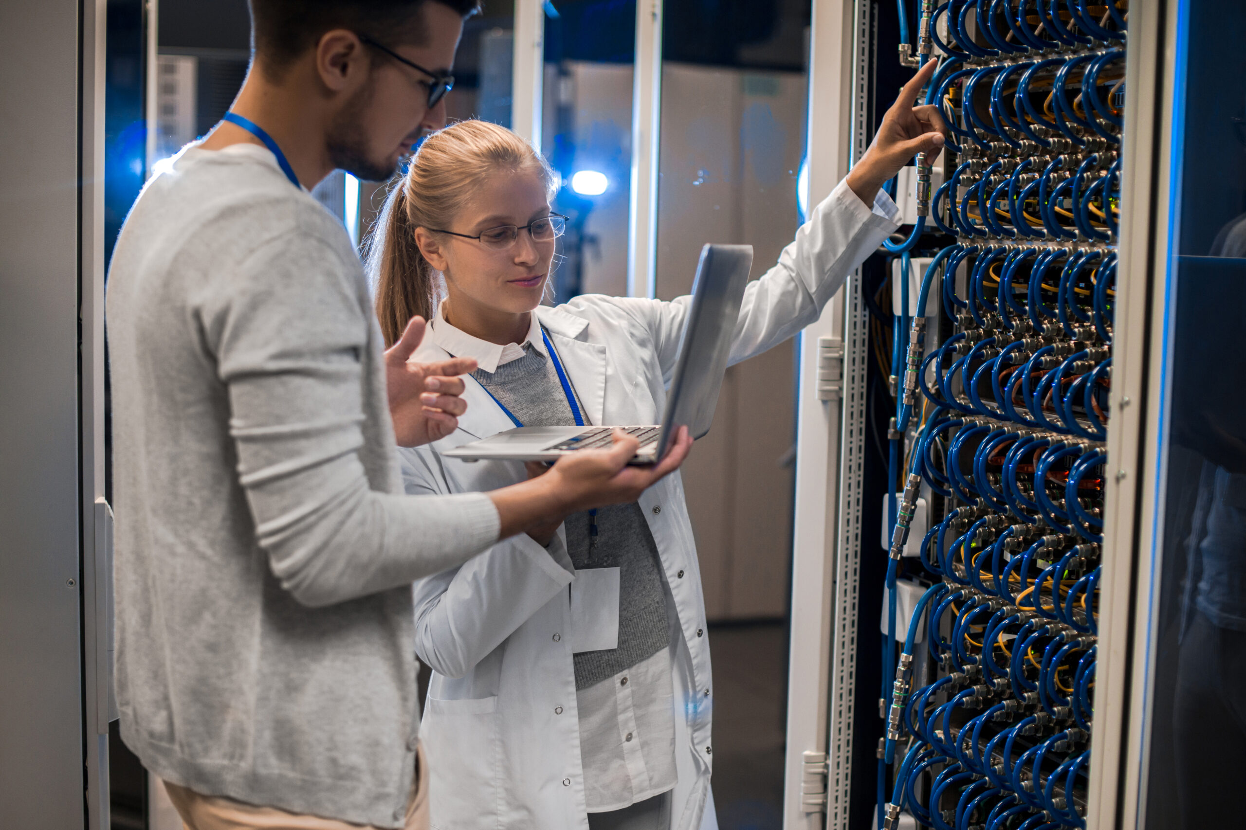 Portrait of young man and woman standing by server cabinets and discussing data while working with supercomputer in IT center